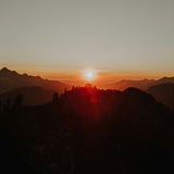 Sunset over mountains with silhouette of trees on a hill